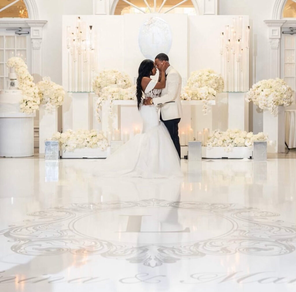 Bride and Groom dressed in all white, embracing each other  lovingly, in an all white decorated room 