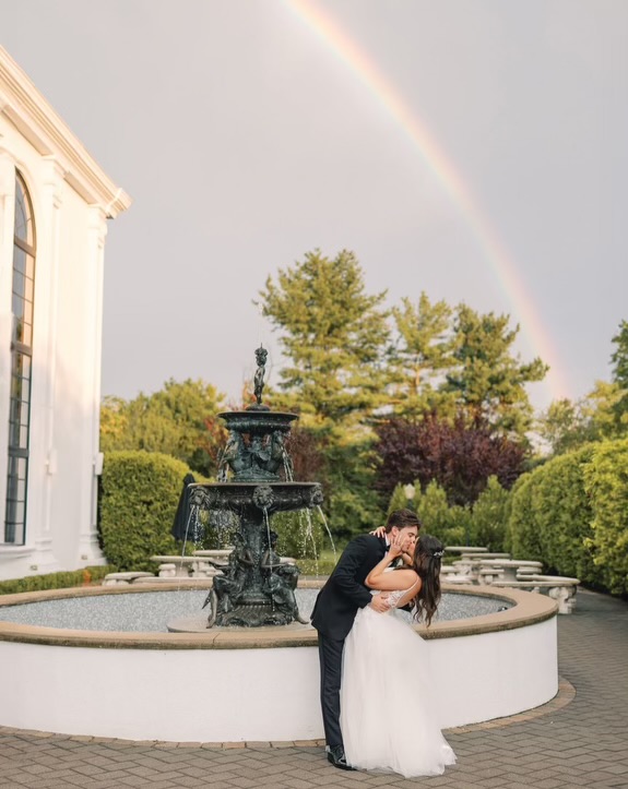 The Addison Park bride and groom kissing by fountain rainbow in sky